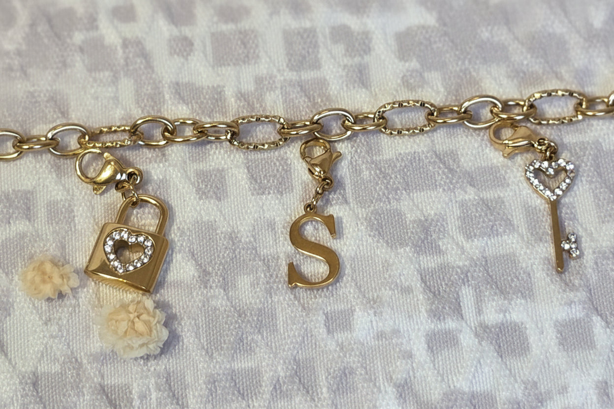Exemple d'un bracelet épais de couleur doré avec 3 Charms, 1 cadenas, a lettre S et une clé en forme de  peur et avec des strass